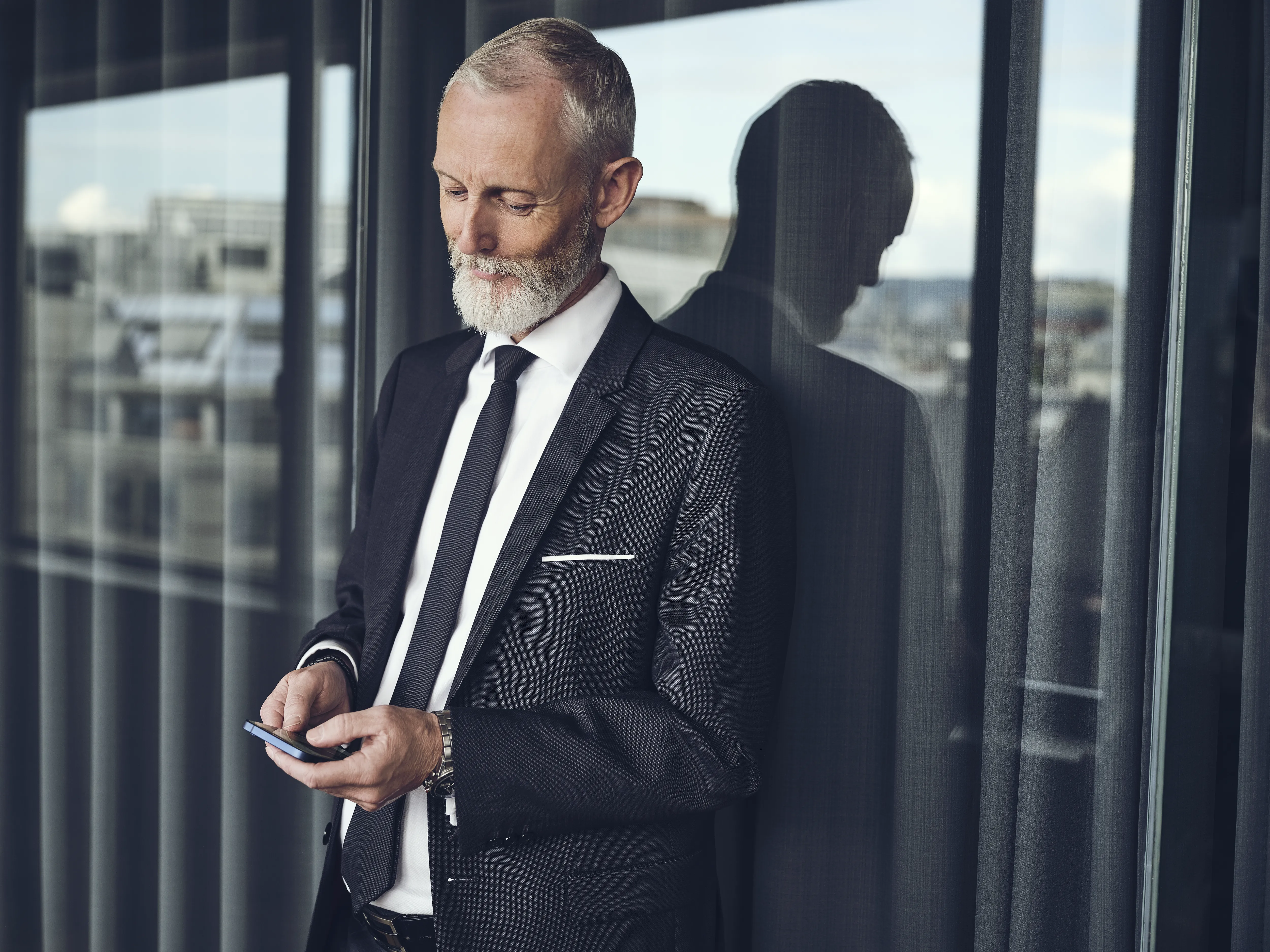 Mann steht am Fenster und schaut auf sein Smartphone