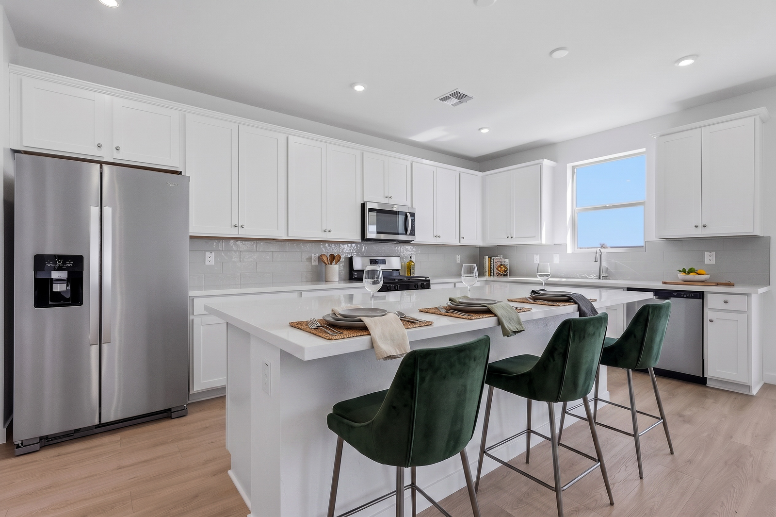 spacious kitchen with white cabinets, quartz countertops, and green barstools