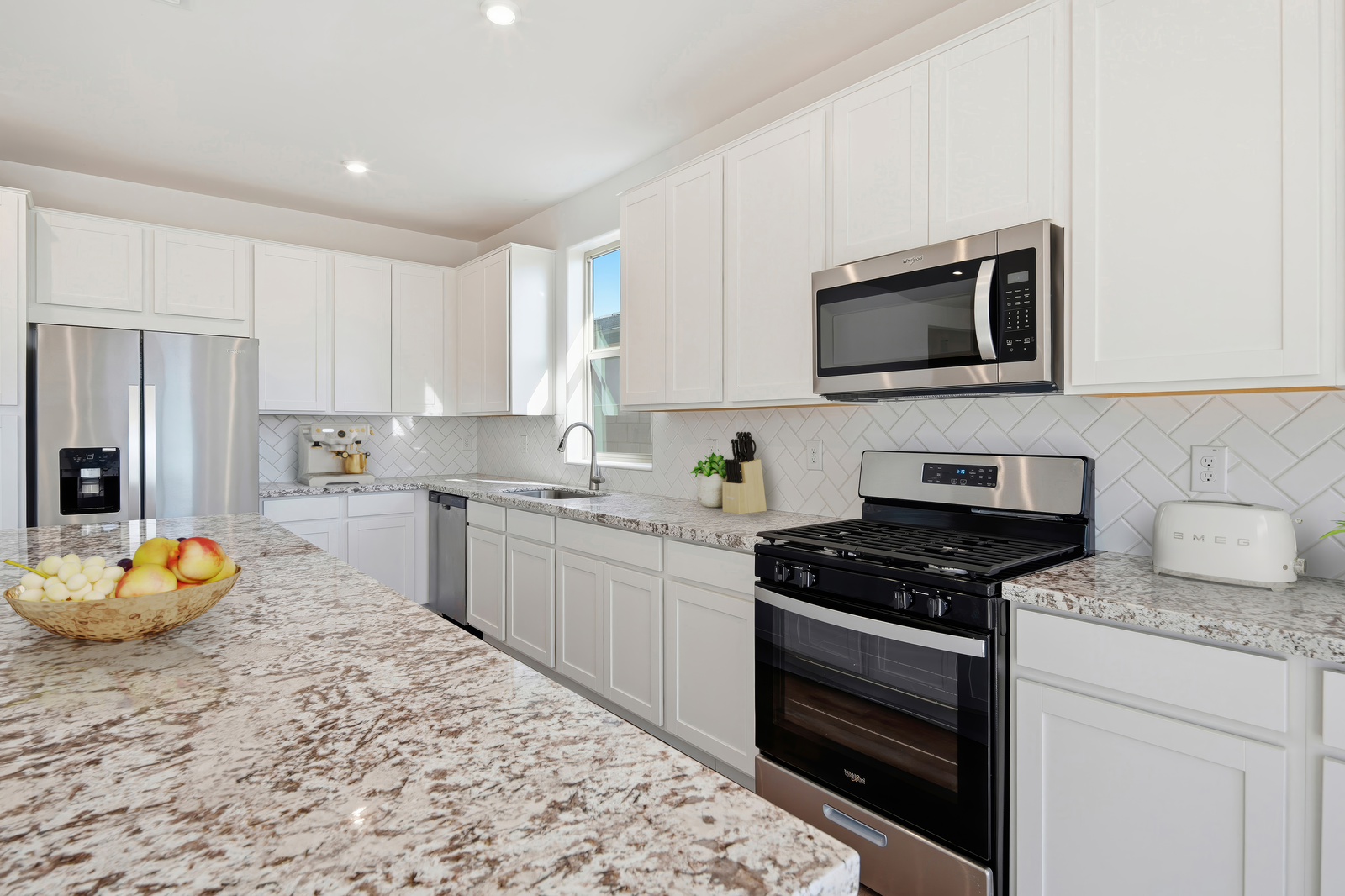 spacious kitchen with a granite countertop, white cabinets, and stainless-steel appliances