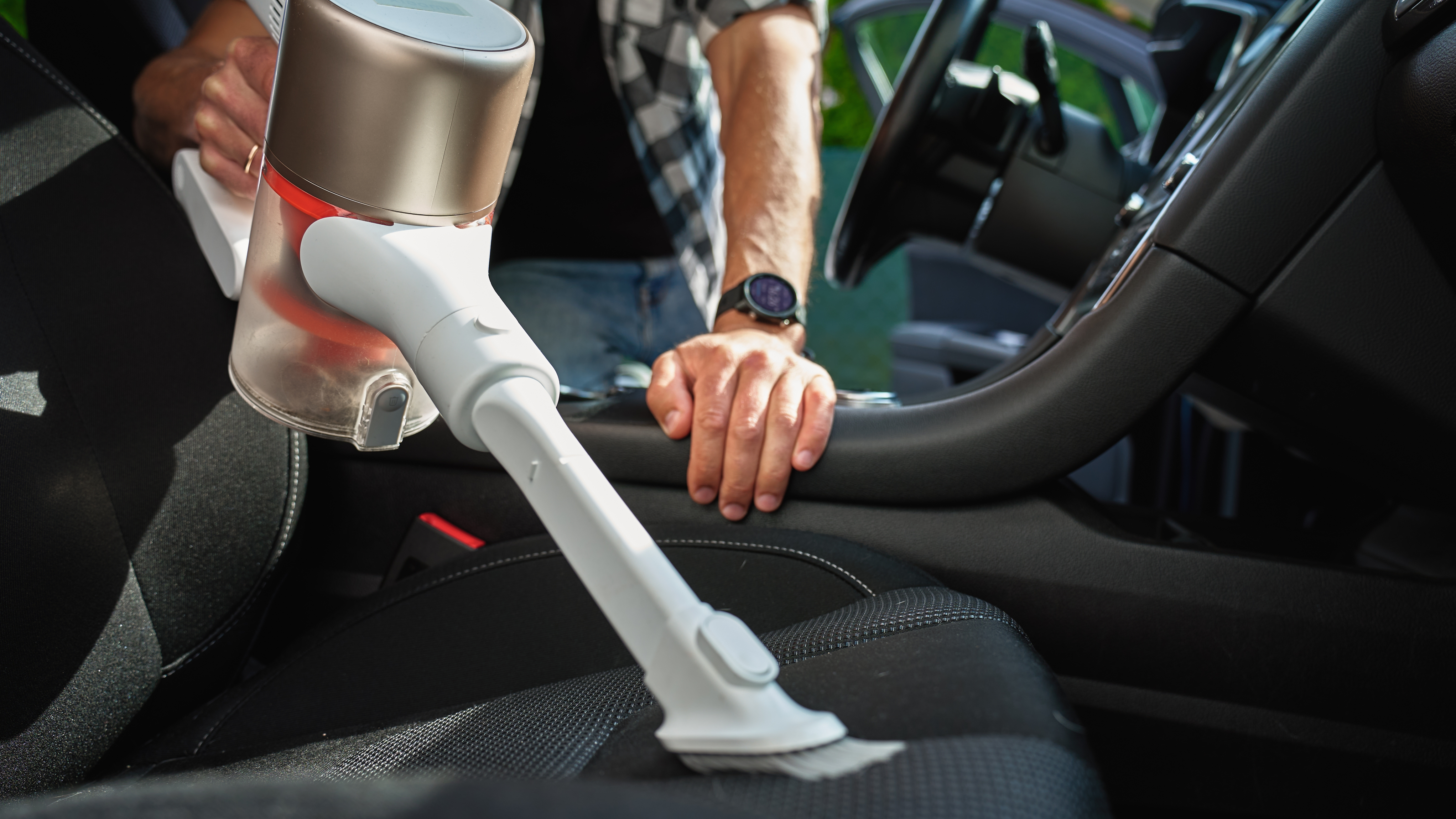 Person using a handheld vacuum cleaner on a car seat.