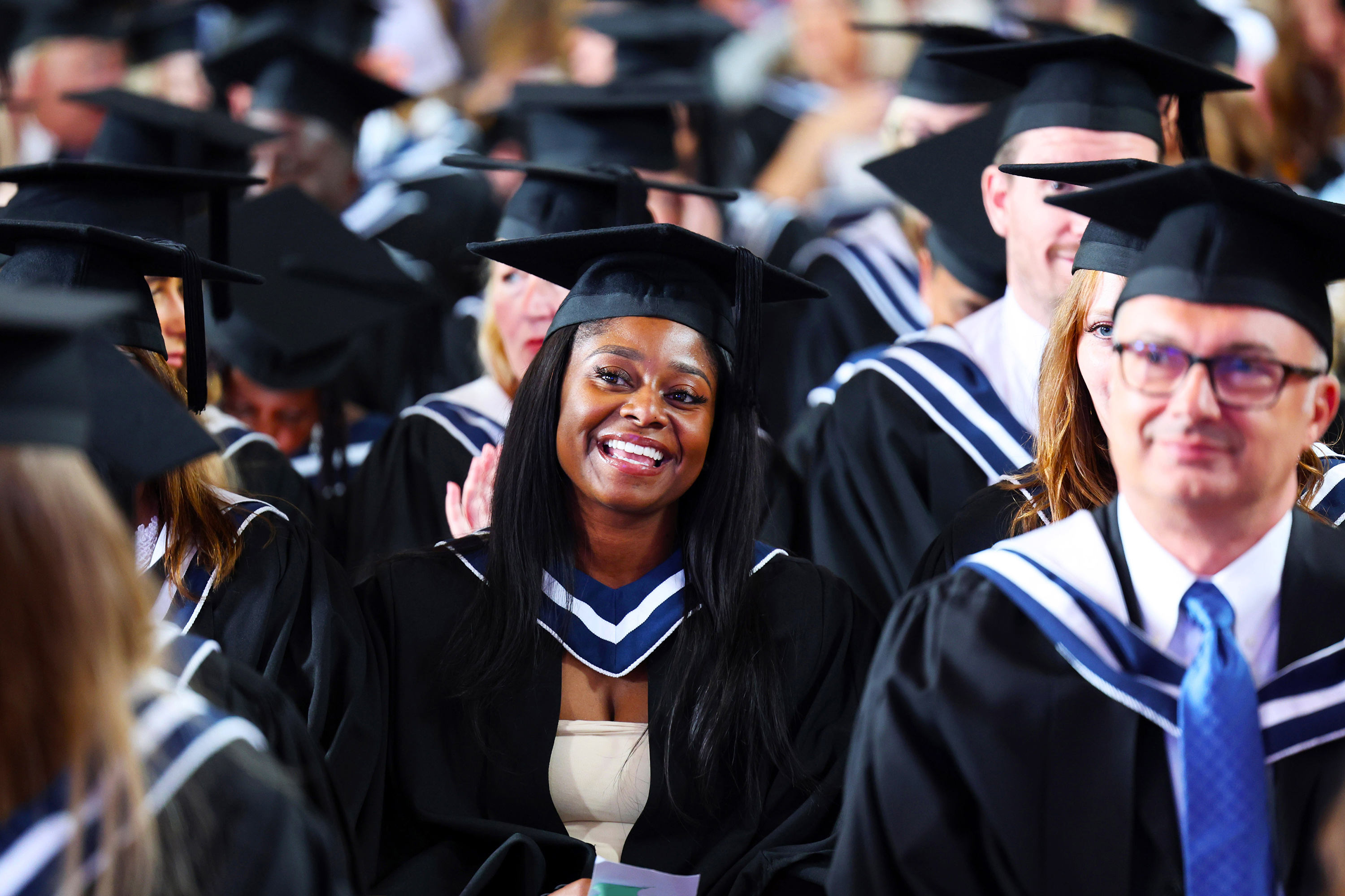 Smiling graduate in cap and gown seated in a crowd