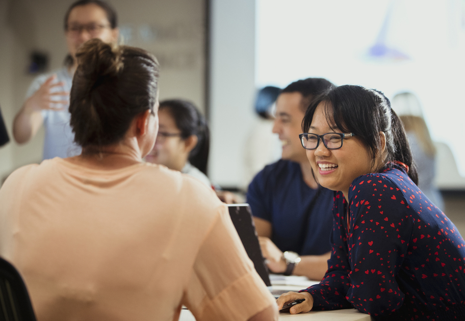 Smiling woman in a navy blouse with red hearts talking to another participant during a workshop discussion.