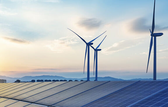 Solar panels in from of wind turbines at sunset