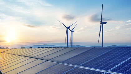 Solar panels in from of wind turbines at sunset