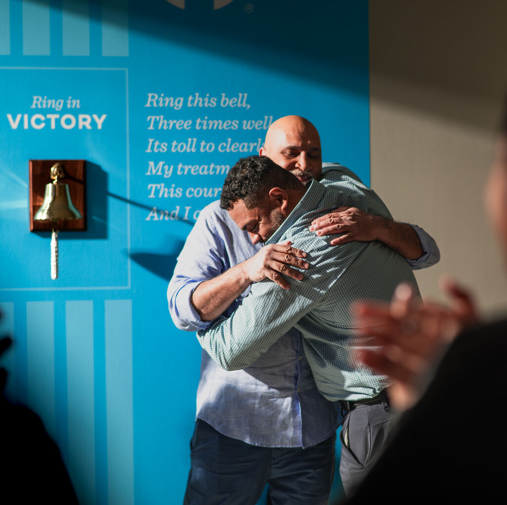 man hugs a patient next to the victory bell