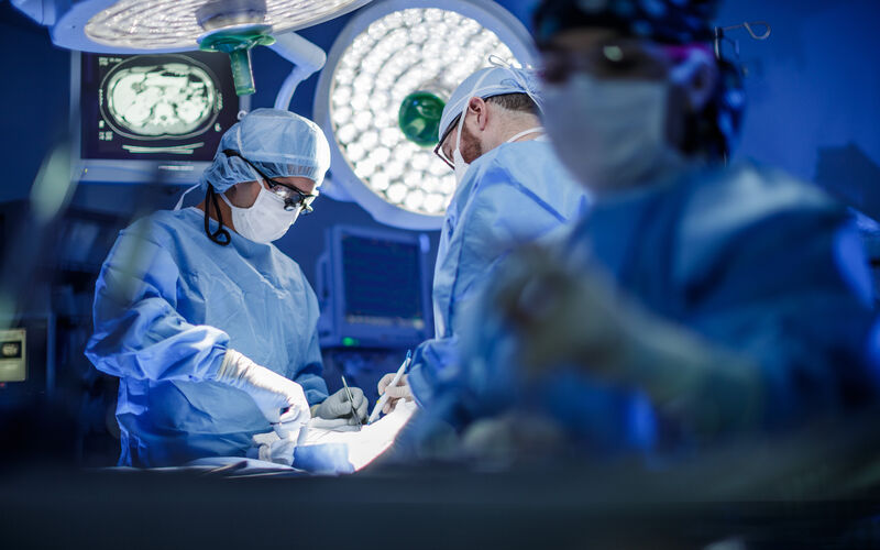 image of a surgical suite with two doctors working on a patient and a nurse off to the side.
