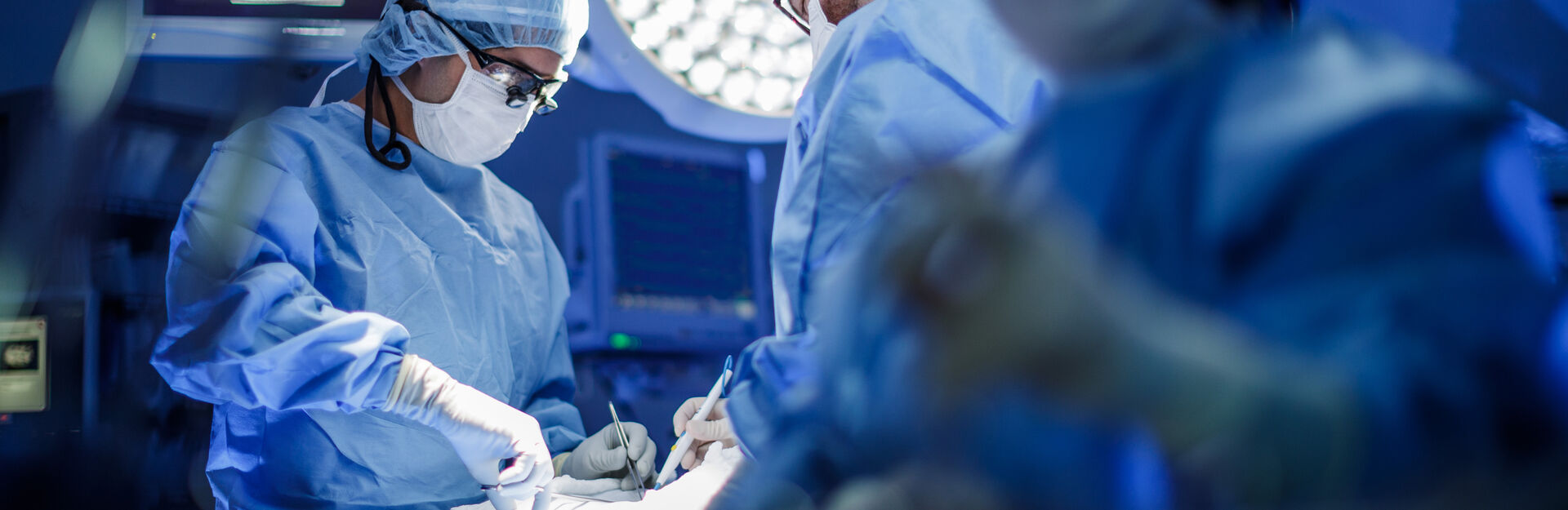 image of a surgical suite with two doctors working on a patient and a nurse off to the side.