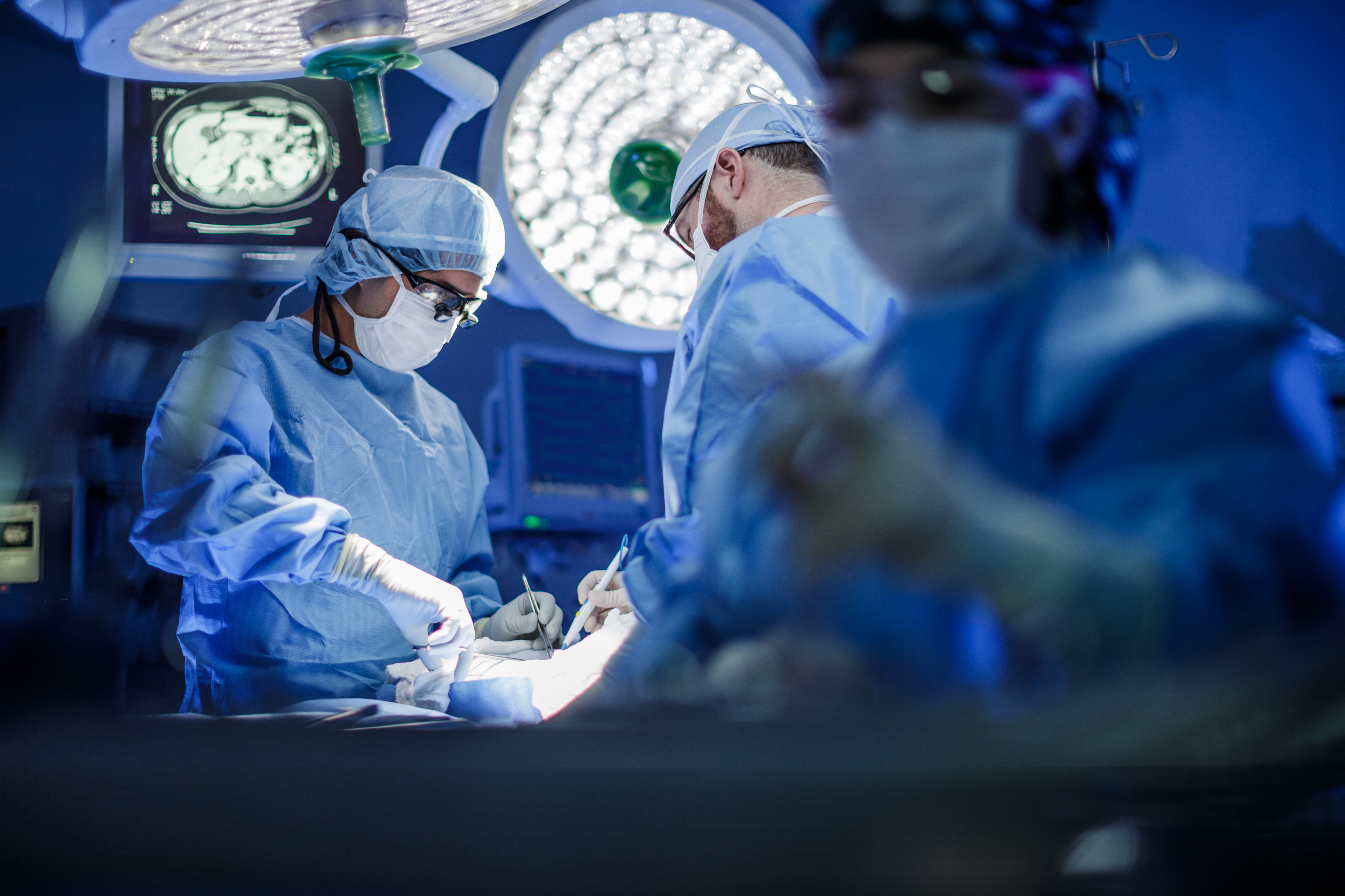 image of a surgical suite with two doctors working on a patient and a nurse off to the side.