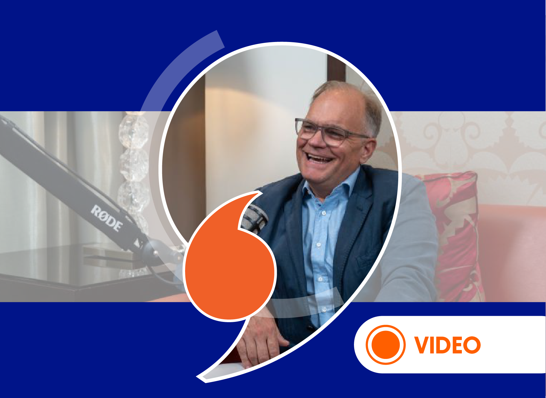 On a dark blue background, a central portrait circle shows a smiling man with glasses, wearing a blue jacket and shirt. An orange speech bubble overlaps the bottom-center of the portrait circle, and a ‘VIDEO’ tag is in the bottom-right corner.