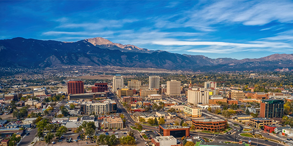 A landscape view of Colorado Springs, CO. The Rocky Mountains rise into the sky behind the city.