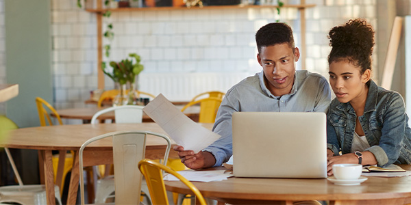 A Black couple sits at a table with papers and a laptop