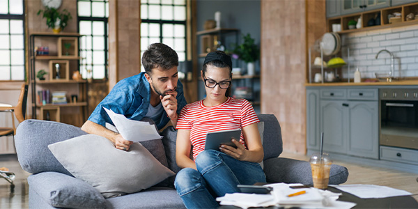 A couple on the couch looks at paperwork and a tablet.