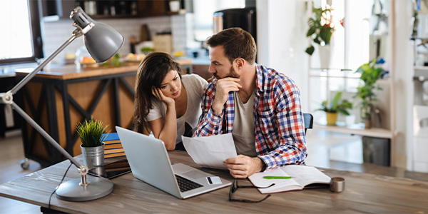 A white couple sits at a table going over paperwork in front of a laptop