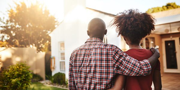A straight, Black couple with their backs to the camera look at a home.