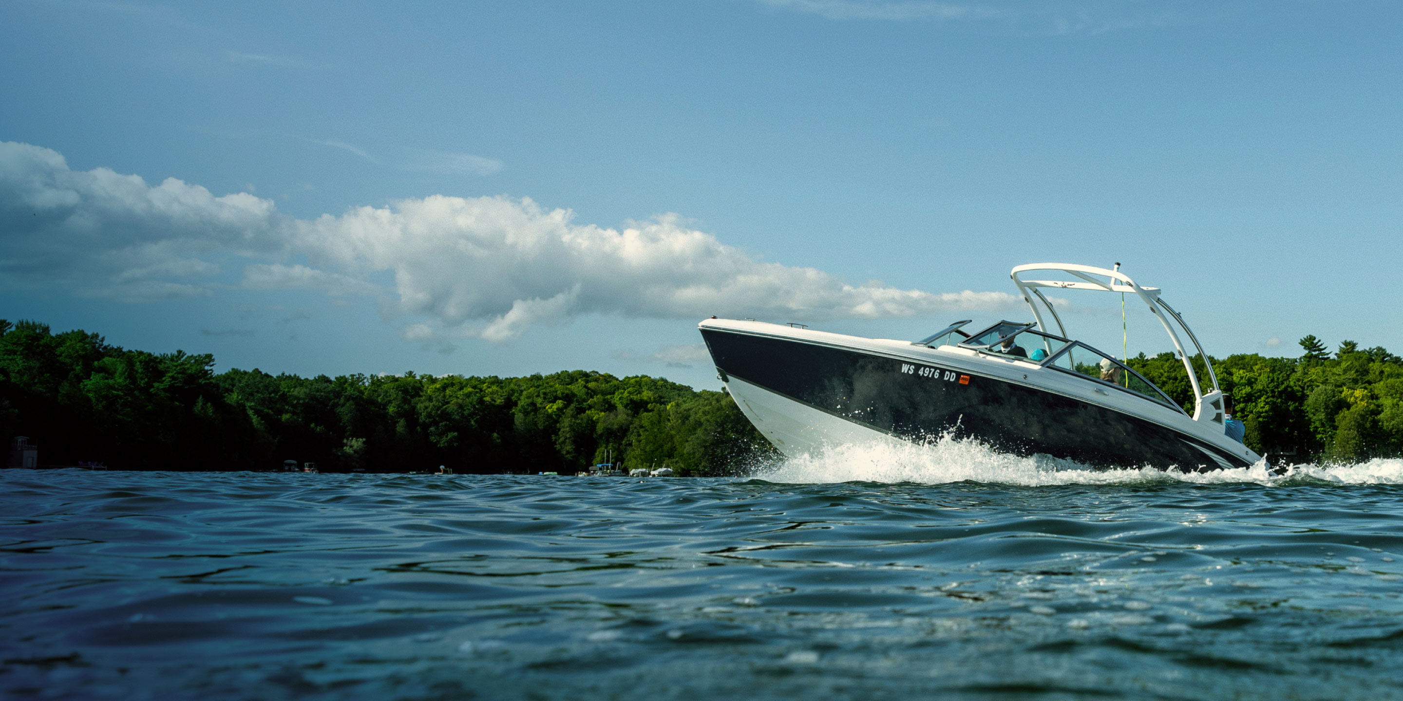 Black and white powerboat accelerates across a lake beneath a summery sky