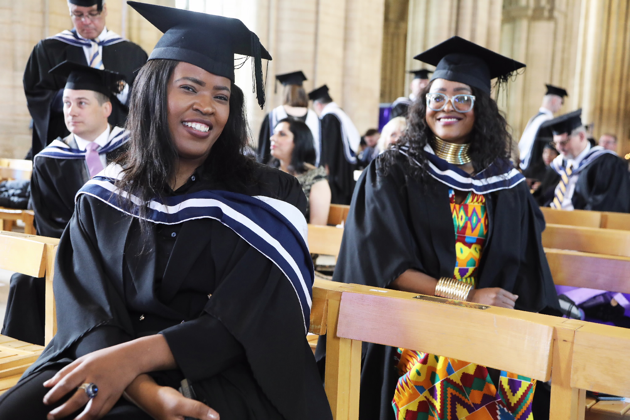 Two female graduates smiling while seated at the ceremony