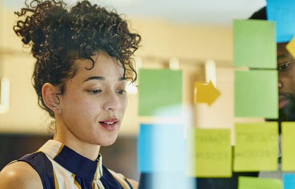 Two business professionals looking at a glass wall of post-it notes