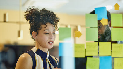 Two business professionals looking at a glass wall of post-it notes