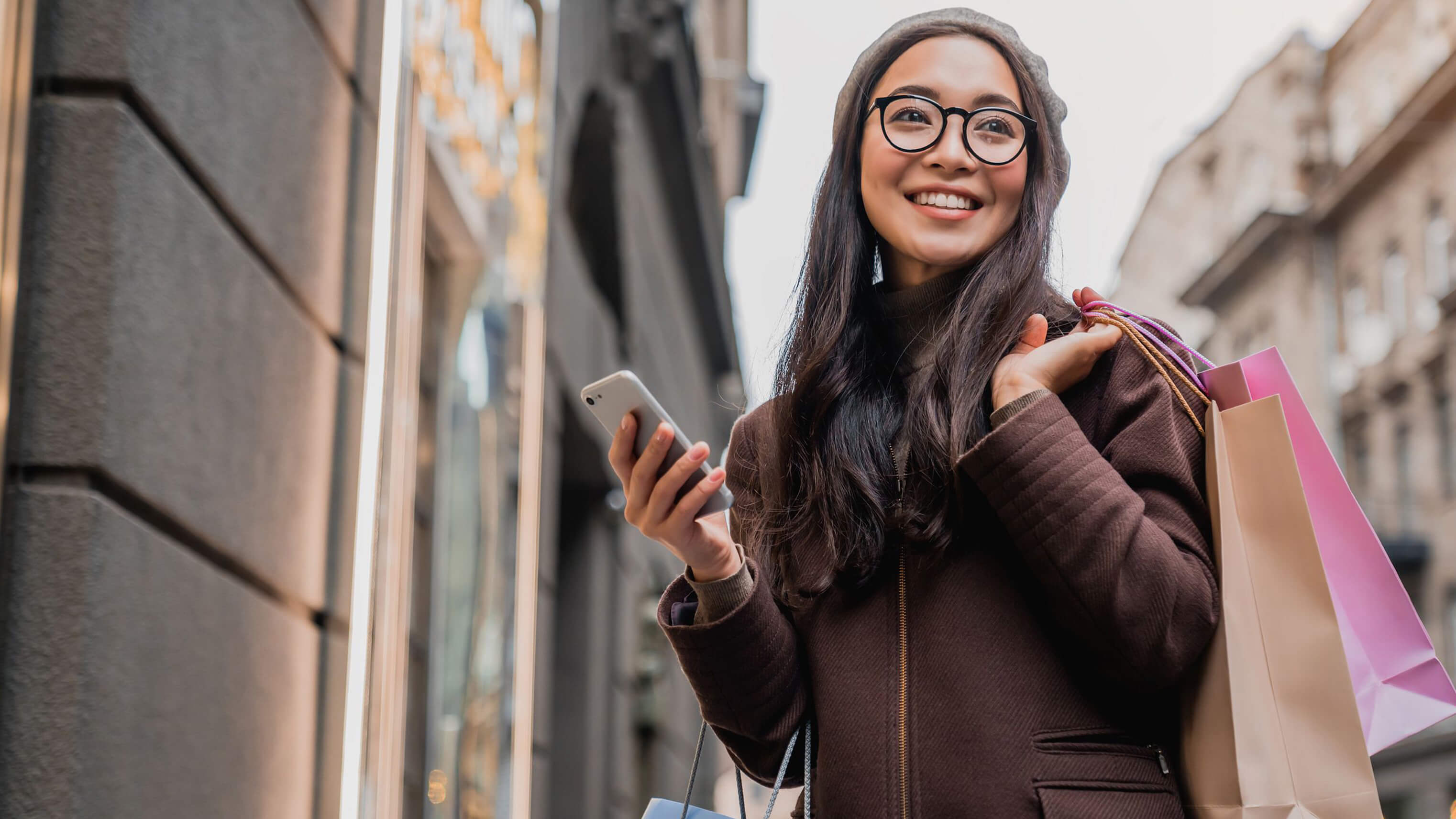 Image of a woman holding a smartphone and shopping bags.