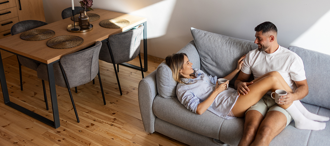 A man and woman sit cuddled on their couch talking