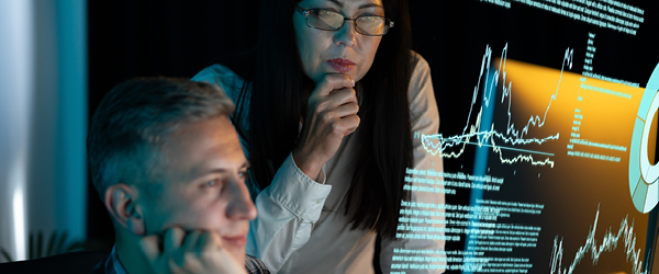 Two people in office looking at a screen with graphs on it 