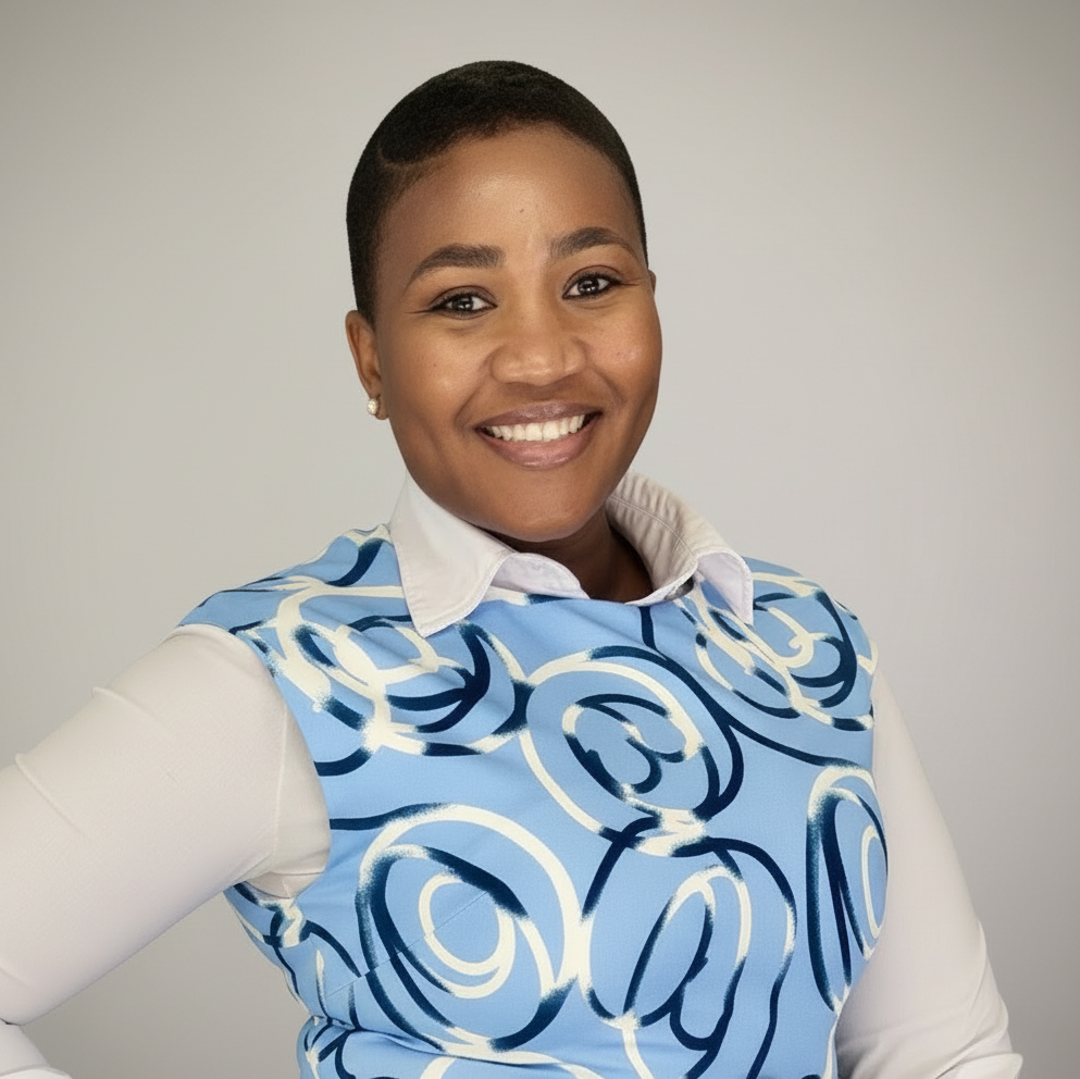 A portrait of a smiling woman with short-cropped dark hair against a neutral grey background. She is wearing a white long-sleeved collared shirt underneath a blue and white patterned vest.