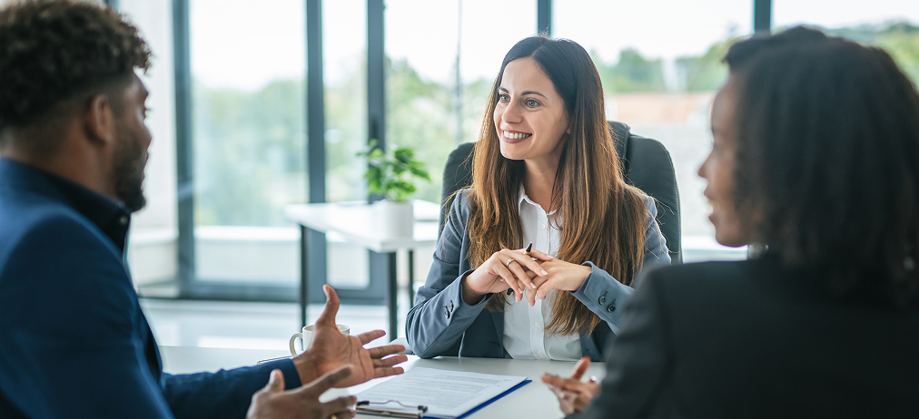 Three colleagues in a workplace meeting around a table.