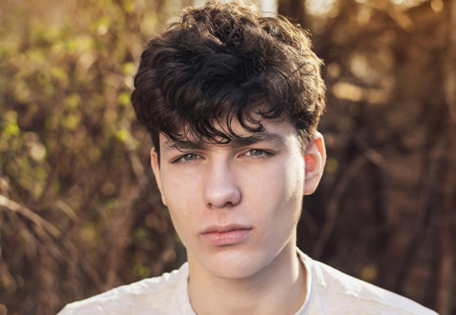 A young man with brown hair looks at the camera with a sullen look on his face. 