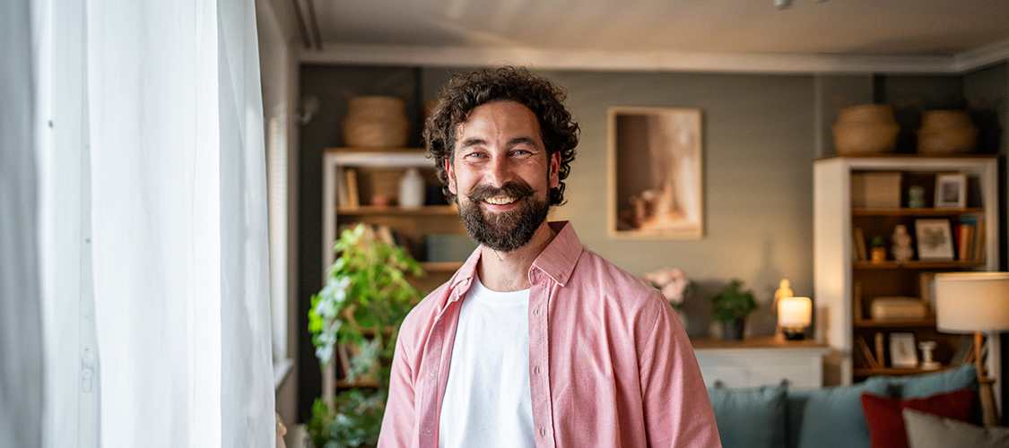 A mixed-race man stands smiling in his living room