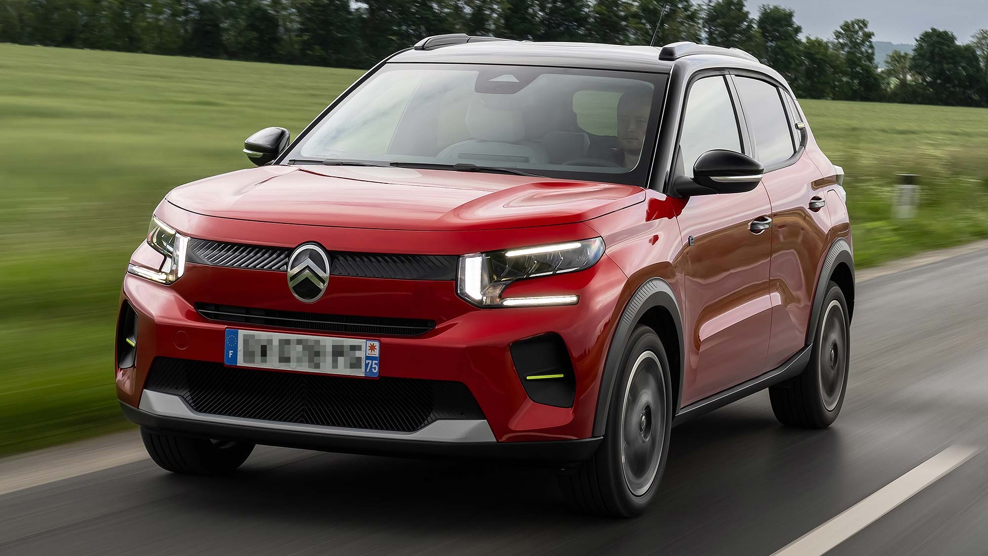 Red Citroën C3 driving on a road through green countryside, with motion blur emphasising movement.