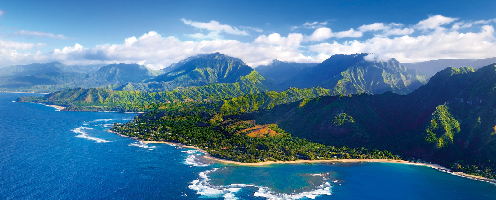 A stunning aerial view of the Hawaii Pacific coast, featuring vibrant blue waters, a lush green shoreline, and majestic mountains in the distance.