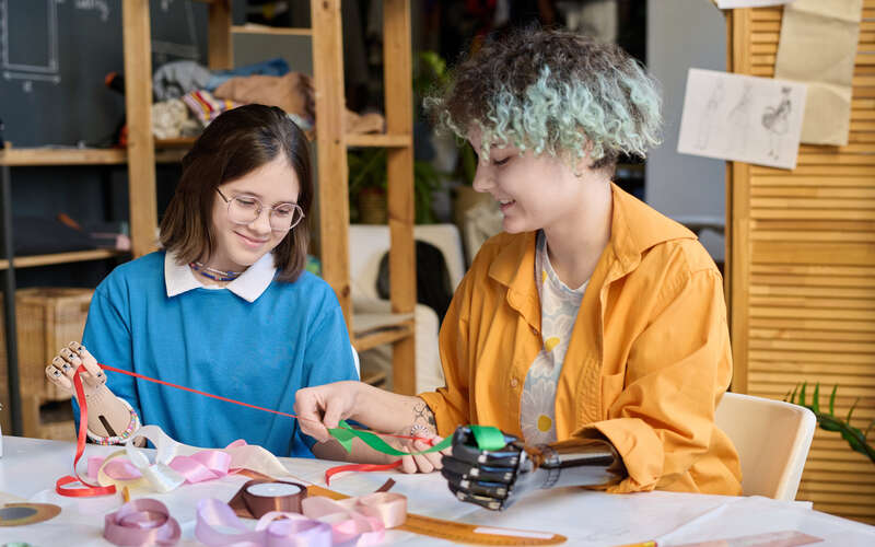 Two teenage girls with prosthetic hands in sewing class.