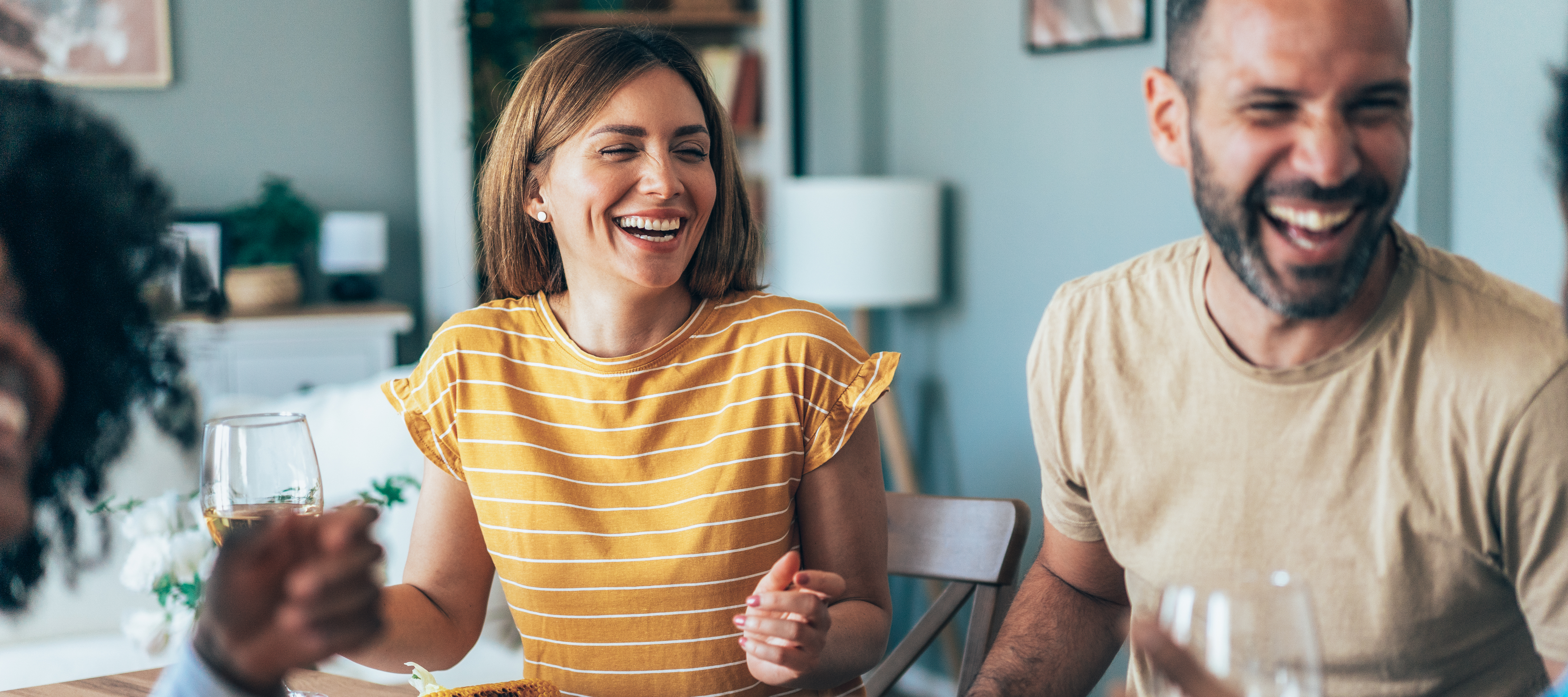 A white woman and man sit laughing with friends around a kitchen table