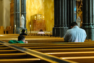 Father praying in church with son looking on.