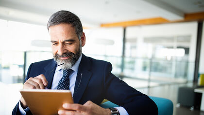 Man in suit looking at a tablet while sitting in a blue armchair 