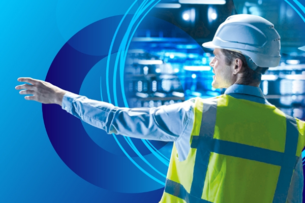 A man in a white hard hat and yellow high-visibility vest stands with his arm outstretched, looking over a high-tech facility, with blue circular graphic overlays.