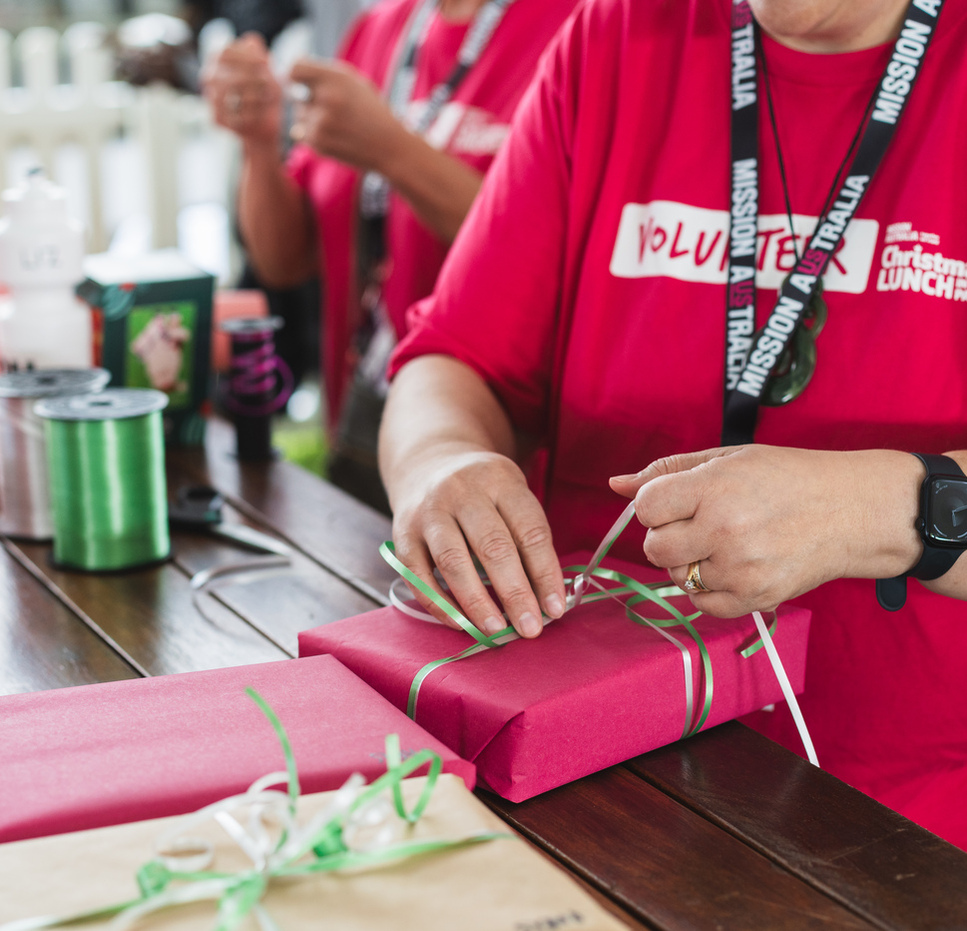 A volunteer carefully gift wraps a Christmas gift at the Christmas Lunch in the Park event.