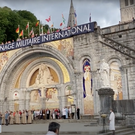 Many people stand outside the pilgrimage center marked with International Military Pilgrimage signage.