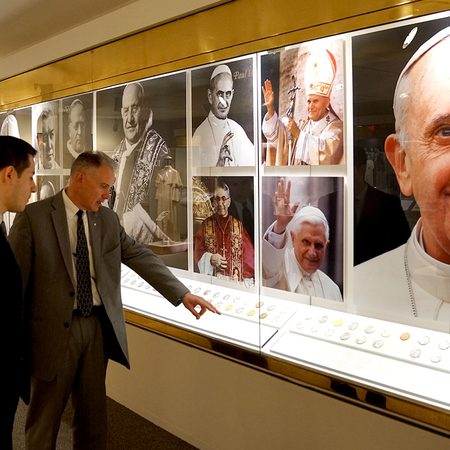 Photo of two men in suits looking at Papal medals in the Papal Gallery of the Blessed Michael McGivney Pilgrimage Center on October 19, 2017. 