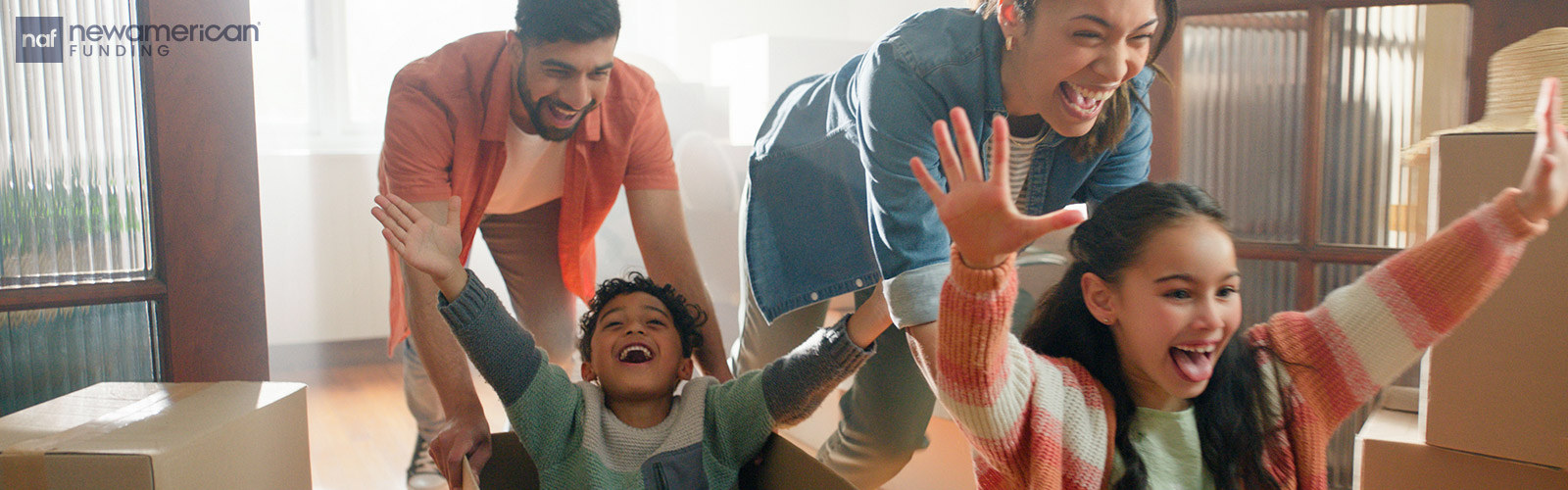 parents pushing their children in moving boxes in their new home