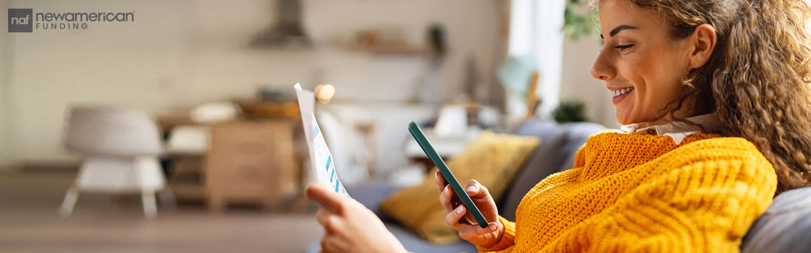 A smiling woman looks at her phone screen and a piece of paper in her hand