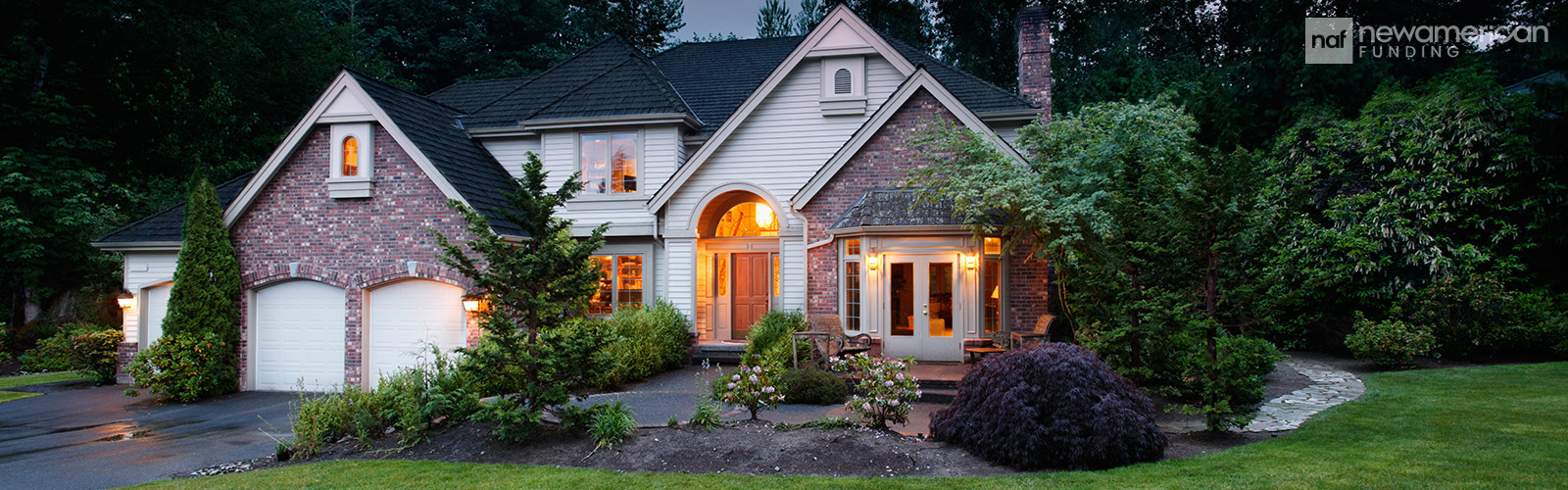 A nice brick and vinyl house with glowing lights on inside and a landscaped yard