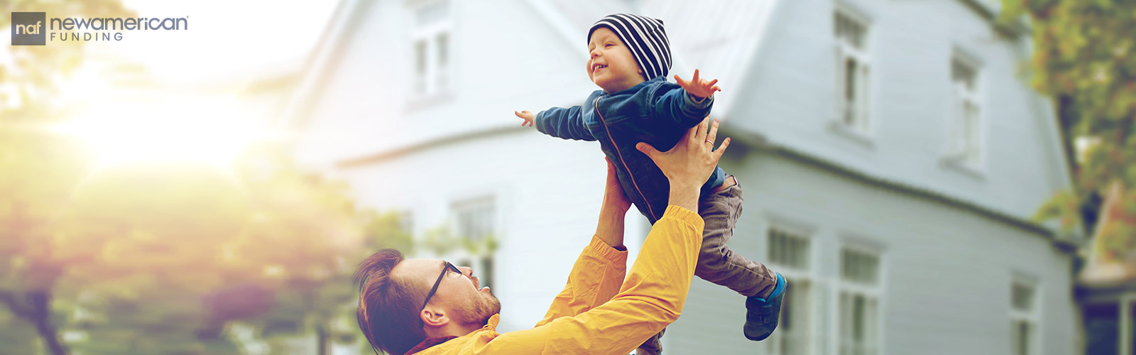 father playfully tossing his son up in front their house