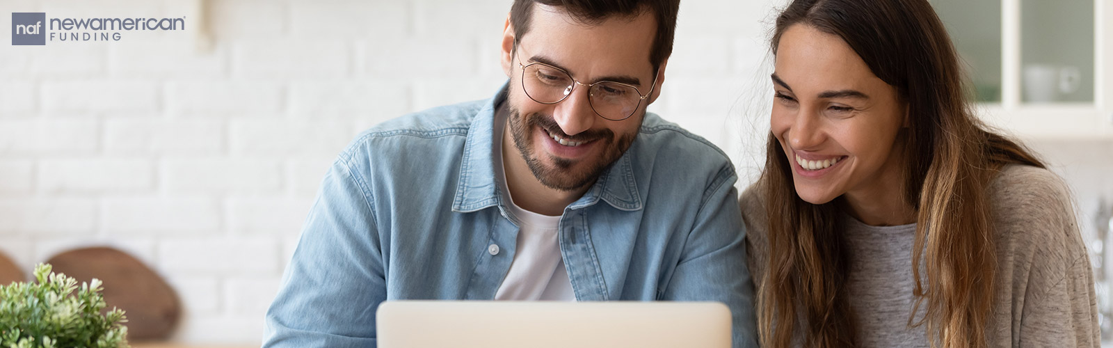 A white man and woman sit and look at their laptop smiling 