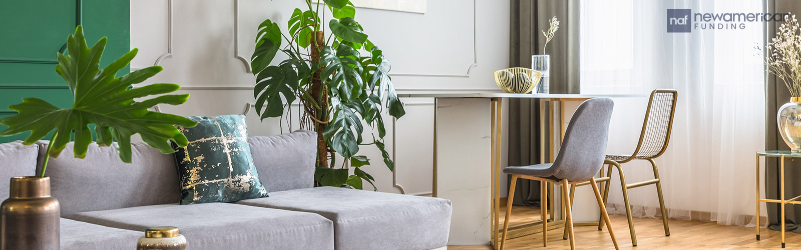 A living room with a simple modern grey couch and small desk with big healthy house plants