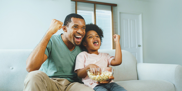A father and small daughter on the couch cheering.