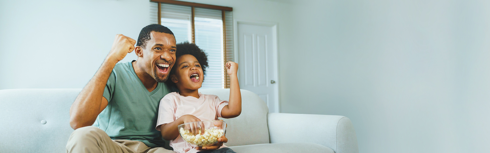 A father and small daughter on the couch cheering.