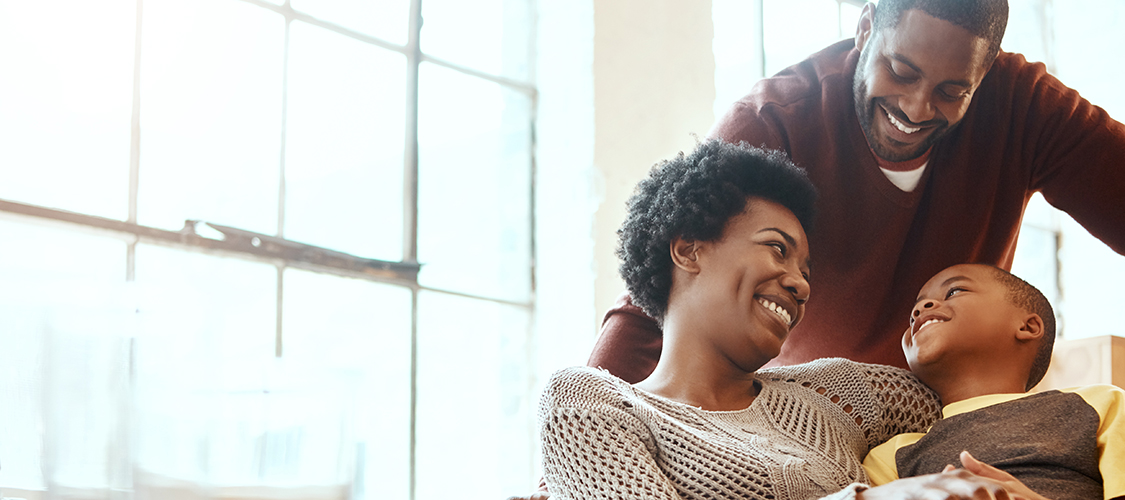 A Black family sits smiling and laughing together on a couch in their home