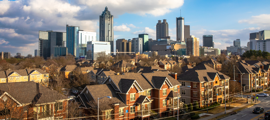 An aerial shot of Atlanta showing blocks of brick homes with skyscrapers behind them.