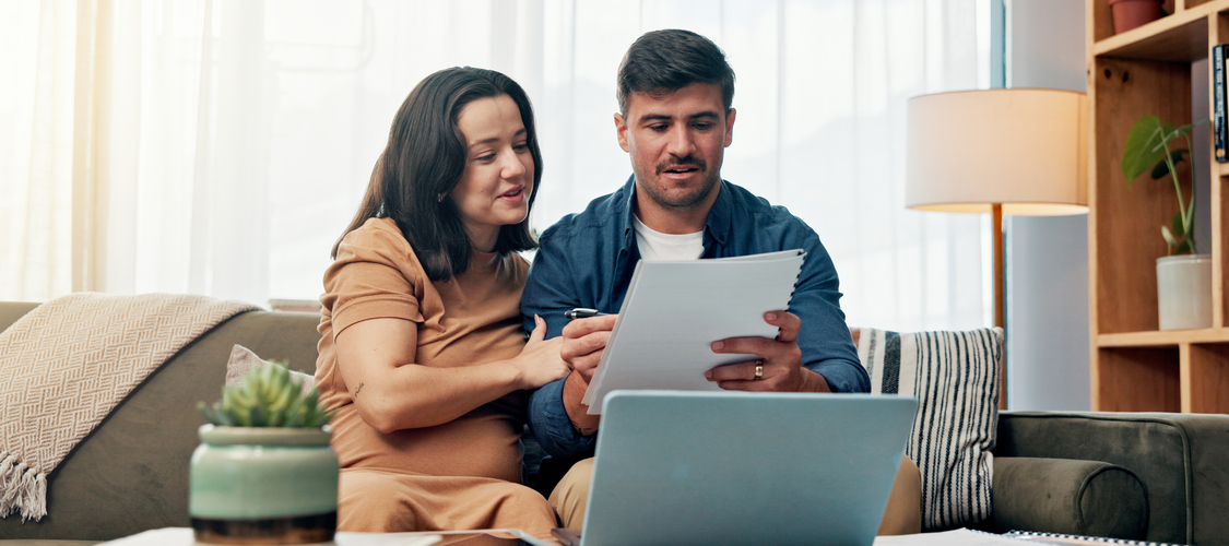 A couple looking at paperwork and a laptop as they sit on a couch.